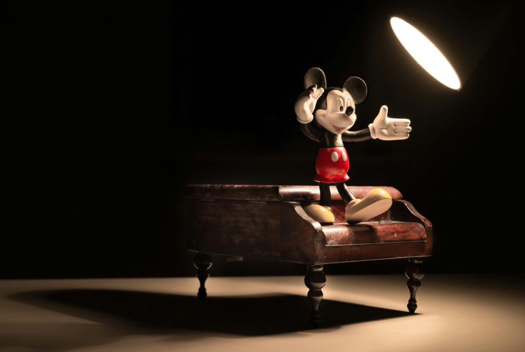 Mickey Mouse figurine poses on a wooden miniature piano under a spotlight.